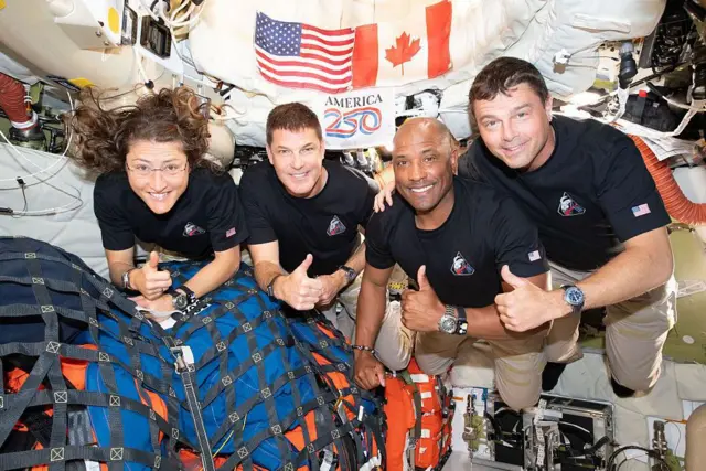 Four members of the Artemis II crew pose with thumbs up as they float in the spacecraft.