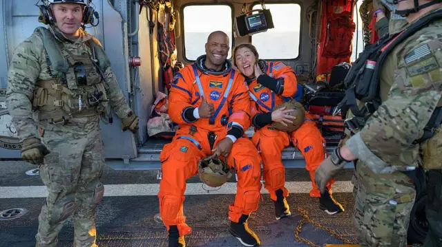 Crew members Christina Koch and Victor Glover smile aboard a rescue craft after being ejected from the Artemis II capsule in the Pacific Ocean.