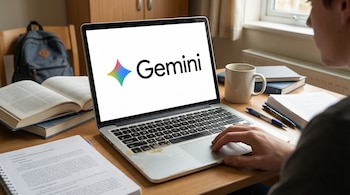 A young man from the right shoulder is using a laptop with the Gemini logo on the screen, surrounded by books, notebooks and a mug on a wooden table.